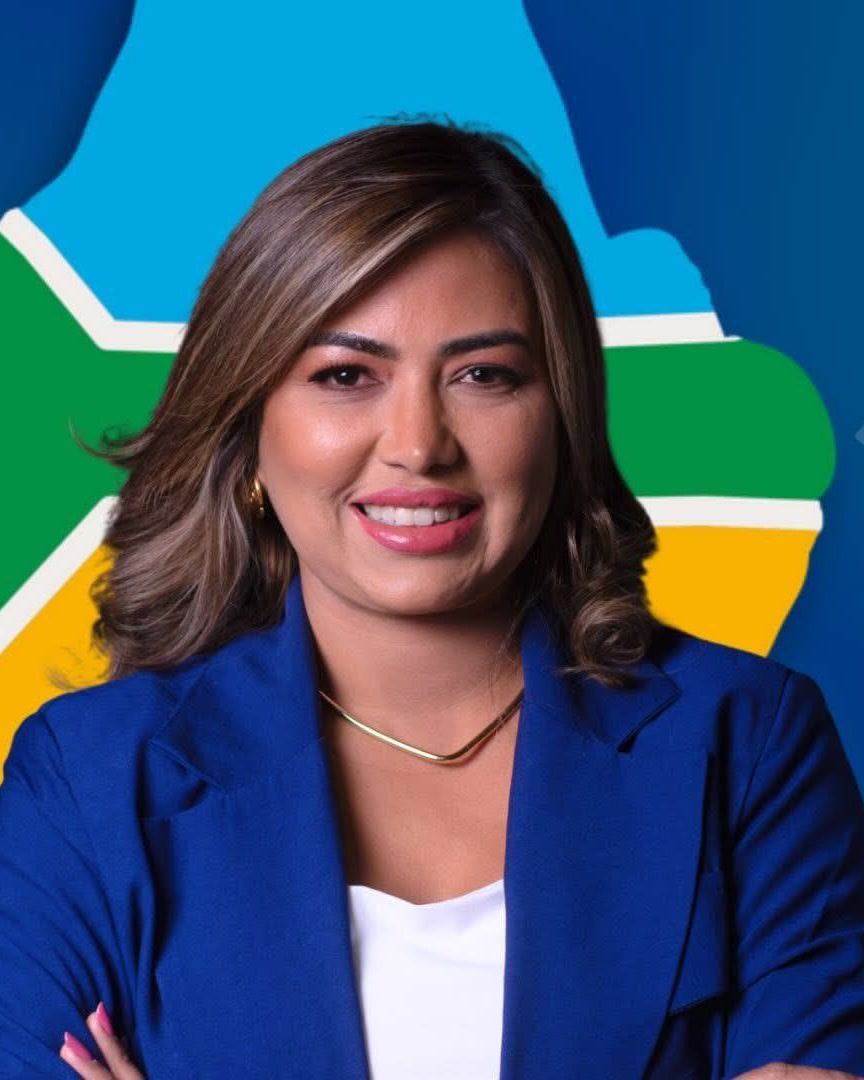 Fotografia oficial de Lucélia Quaresma, de blazer azul, sorrindo, diante da estrela do mapa do Amapá